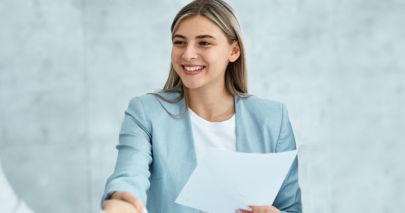 Smiling businesswoman shaking hands while holding a job offer